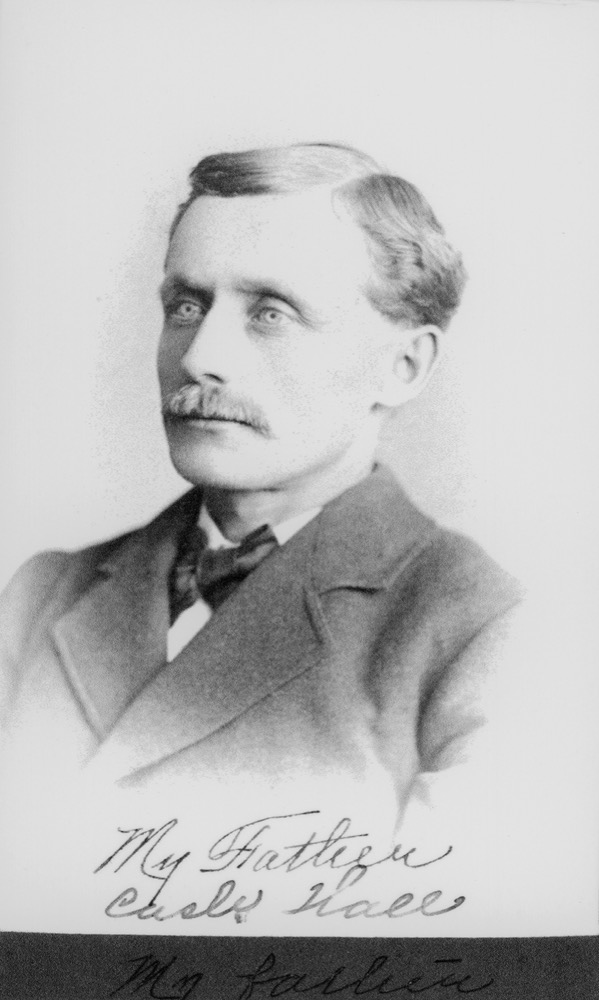 Studio portrait of a man with a mustache in a dark suit and tie. Handwritten beneath: My Father, Cash Hall.